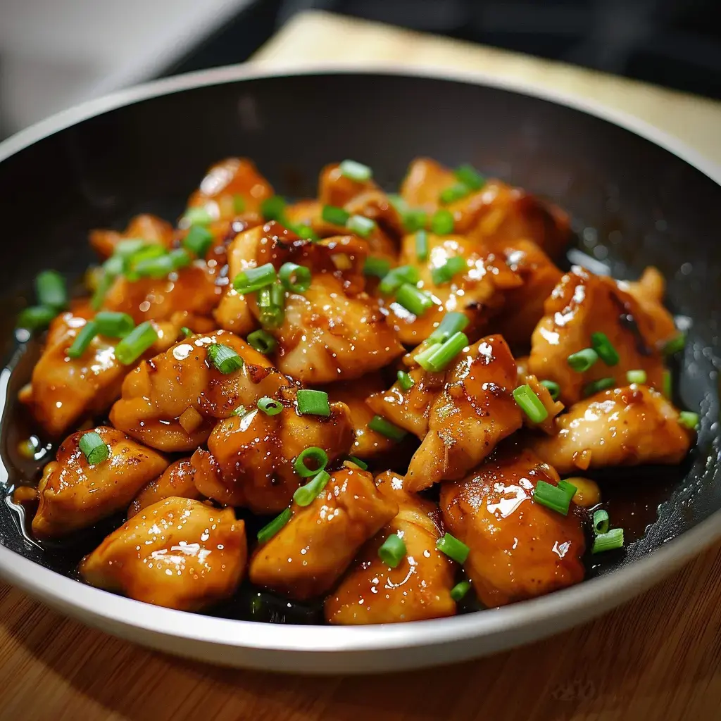 Ein Gericht mit sautiertem Poulet in süßer Sauce, garniert mit gehacktem Schnittlauch, serviert in einer schwarzen Schale.
