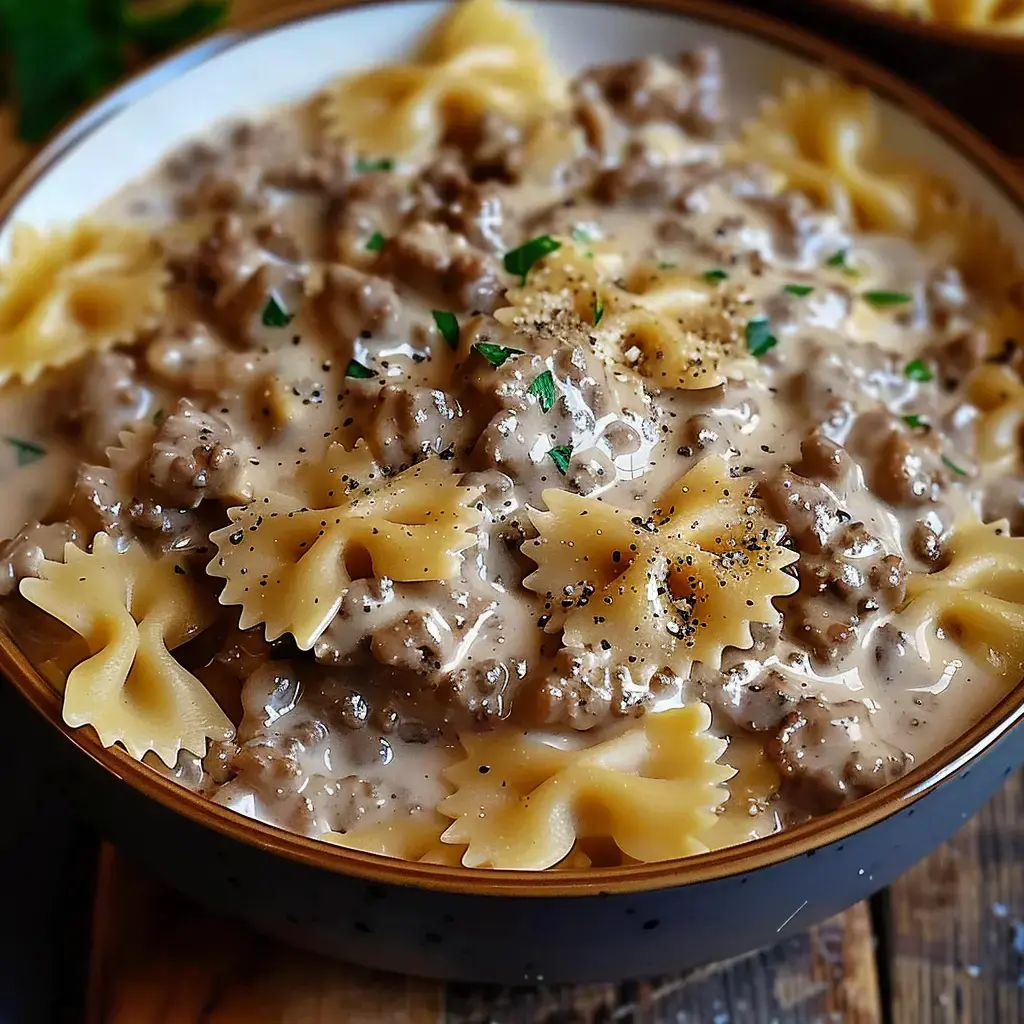 Eine Schüssel Farfalle-Nudeln in einer sahnigen Hackfleischsauce, garniert mit Pfeffer und Petersilie.