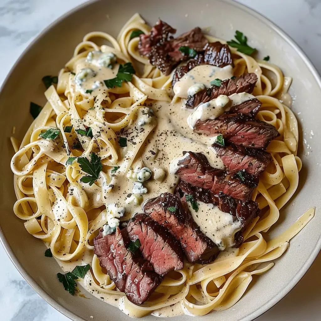 Ein Teller Fettuccine mit Steakscheiben und cremiger Sauce, garniert mit Petersilie und Blauschimmelkäse.