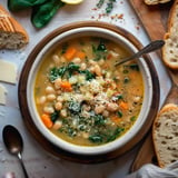 Eine Schüssel weiße Bohnensuppe mit Spinat und Karotten, garniert mit geriebenem Käse und serviert mit knusprigem Brot.