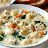 Ein Teller cremige Suppe mit Gnocchi, Hühnerstücken, Karotten und Spinat.